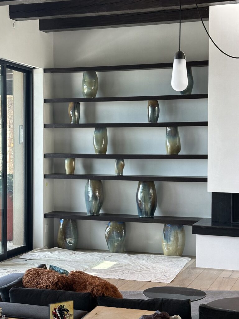 Wall of dark wooden shelves displaying multiple tall ceramic vases in a modern living room.