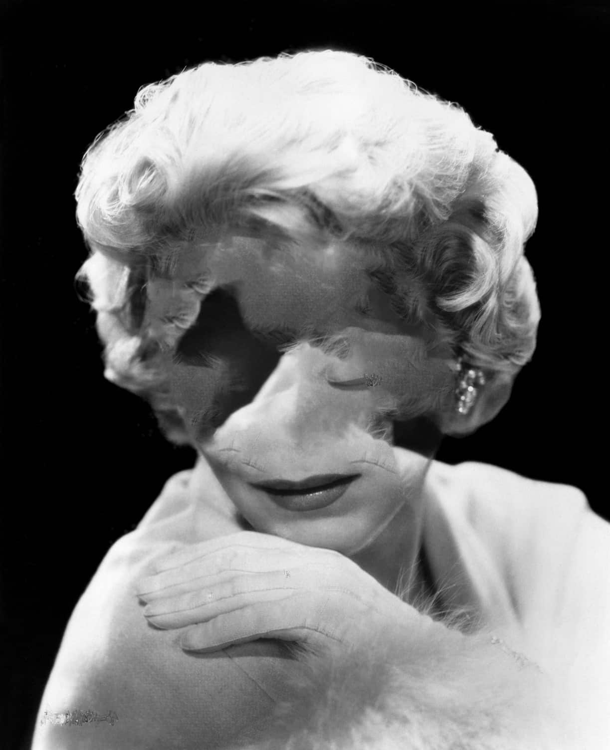 Black-and-white portrait of a woman with curled blonde hair and jewelry, digitally altered so her facial features are obscured and distorted by blurred textures.