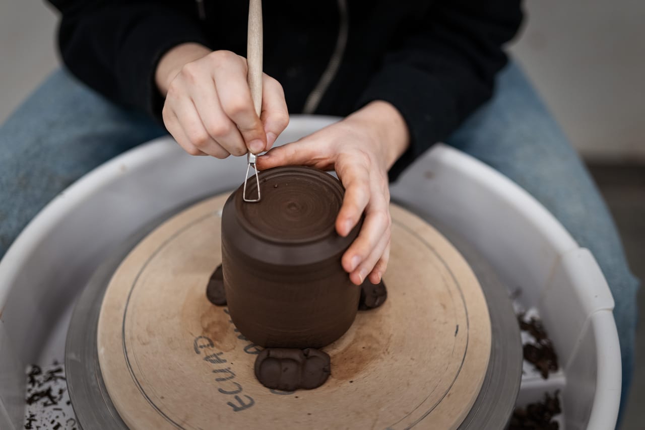 Student shaping clay on pottery wheel in ceramics studio.