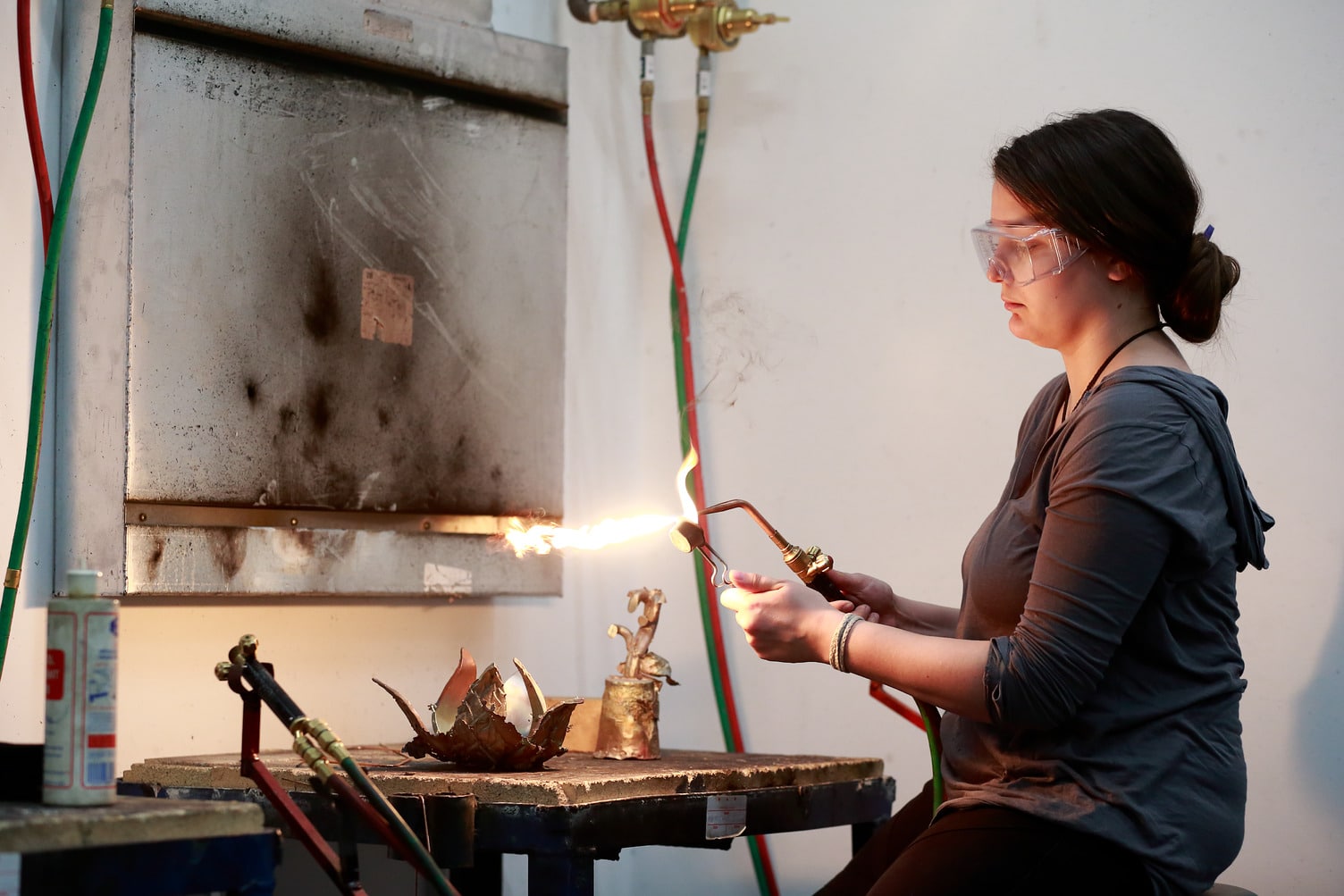 Student wearing safety goggles using a blowtorch to heat metal in a workshop.
