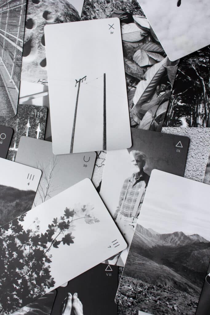 Black-and-white photographic tarot cards scattered on a surface, featuring images of landscapes, objects and people.