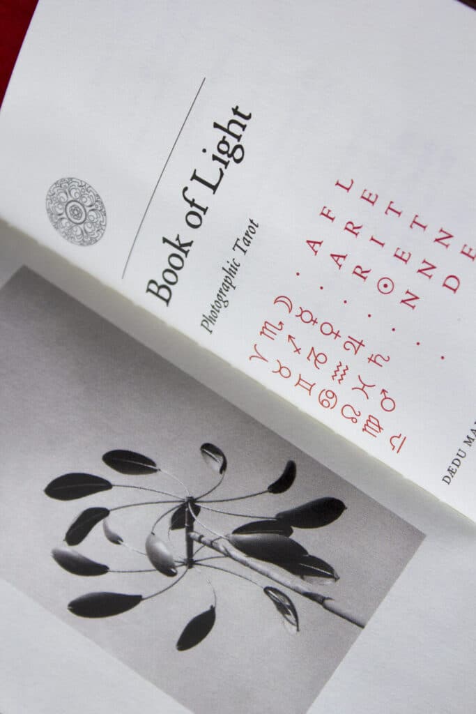 An open book titled Book of Light: Photographic Tarot showing a page with symbols and a black-and-white weathervane photograph