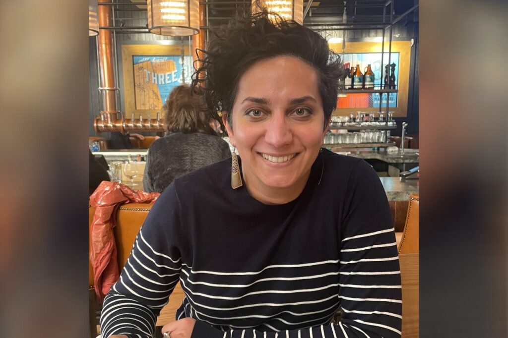 Person with short curly hair smiling at a restaurant table.