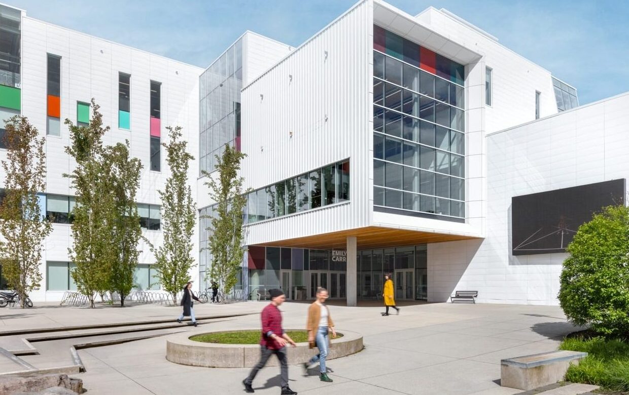 A man and a woman walking in front of the main ECU campus building on a sunny day.