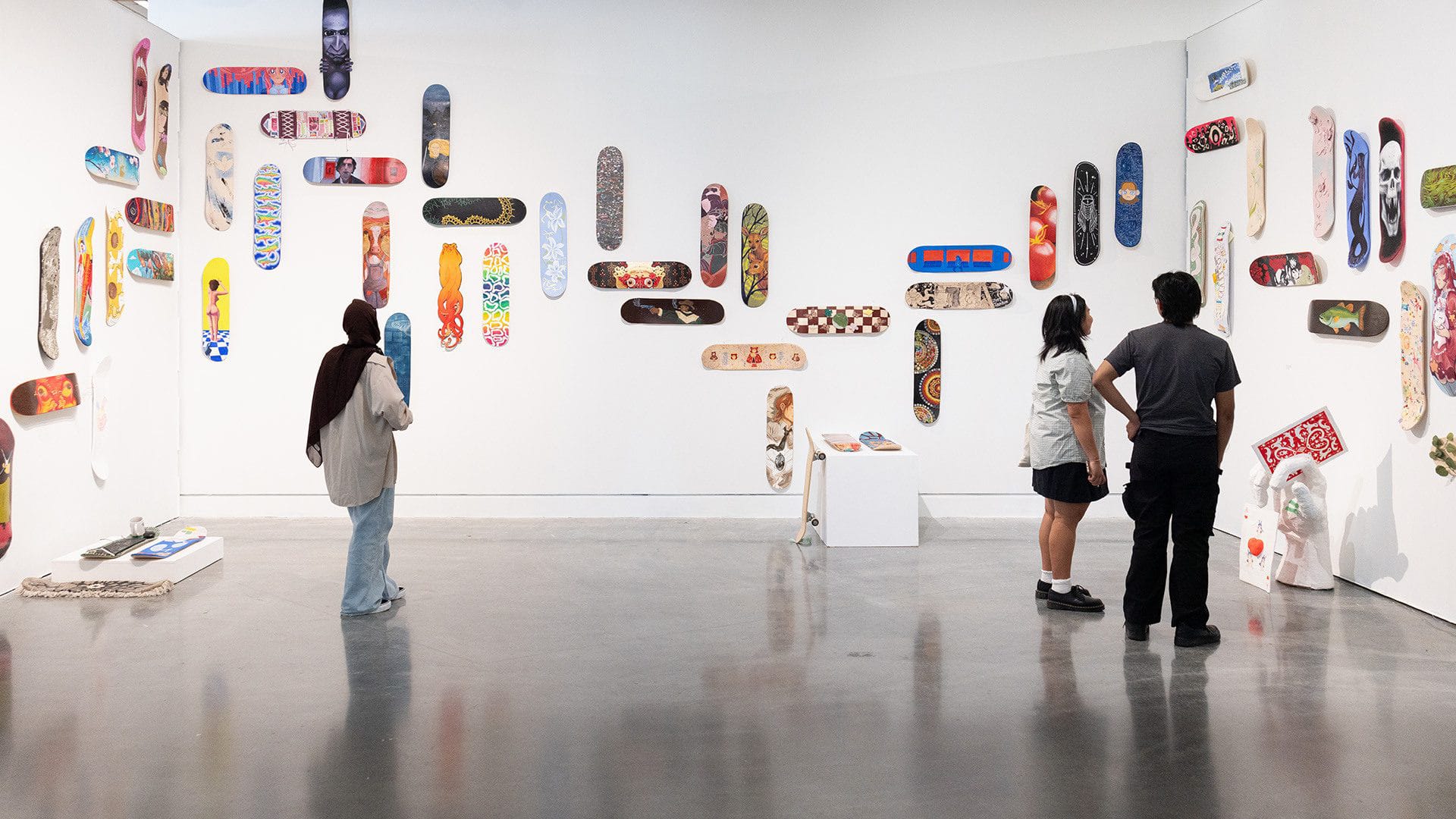 People view a gallery wall filled with skateboard decks, each painted with unique and colorful artwork.