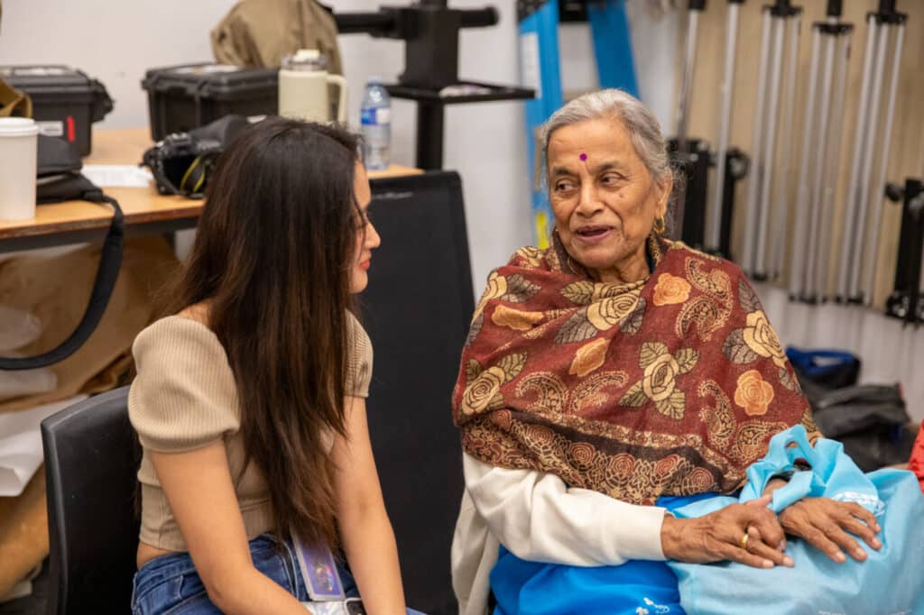 Two people of different generations sit indoors, smiling and talking together.