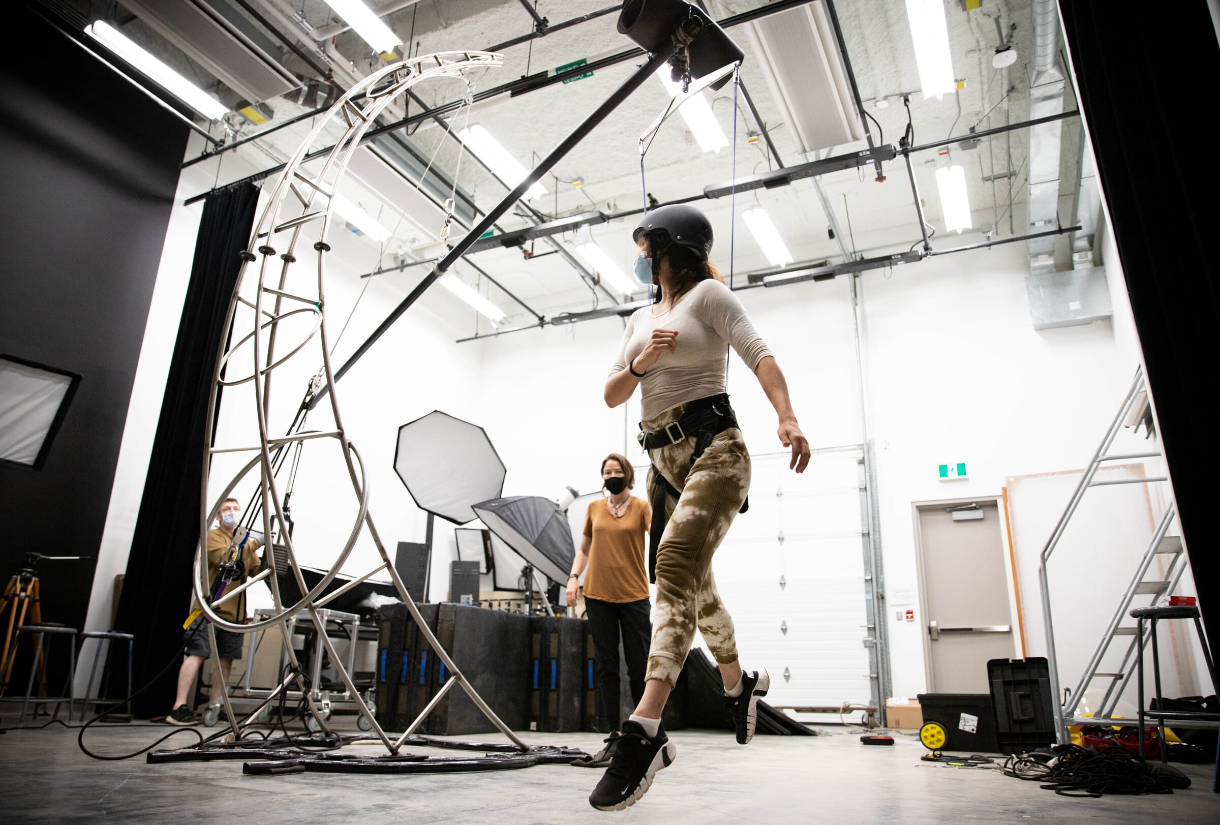 Motion capture studio with white walls and overhead lighting. A suspending woman runs in the air.