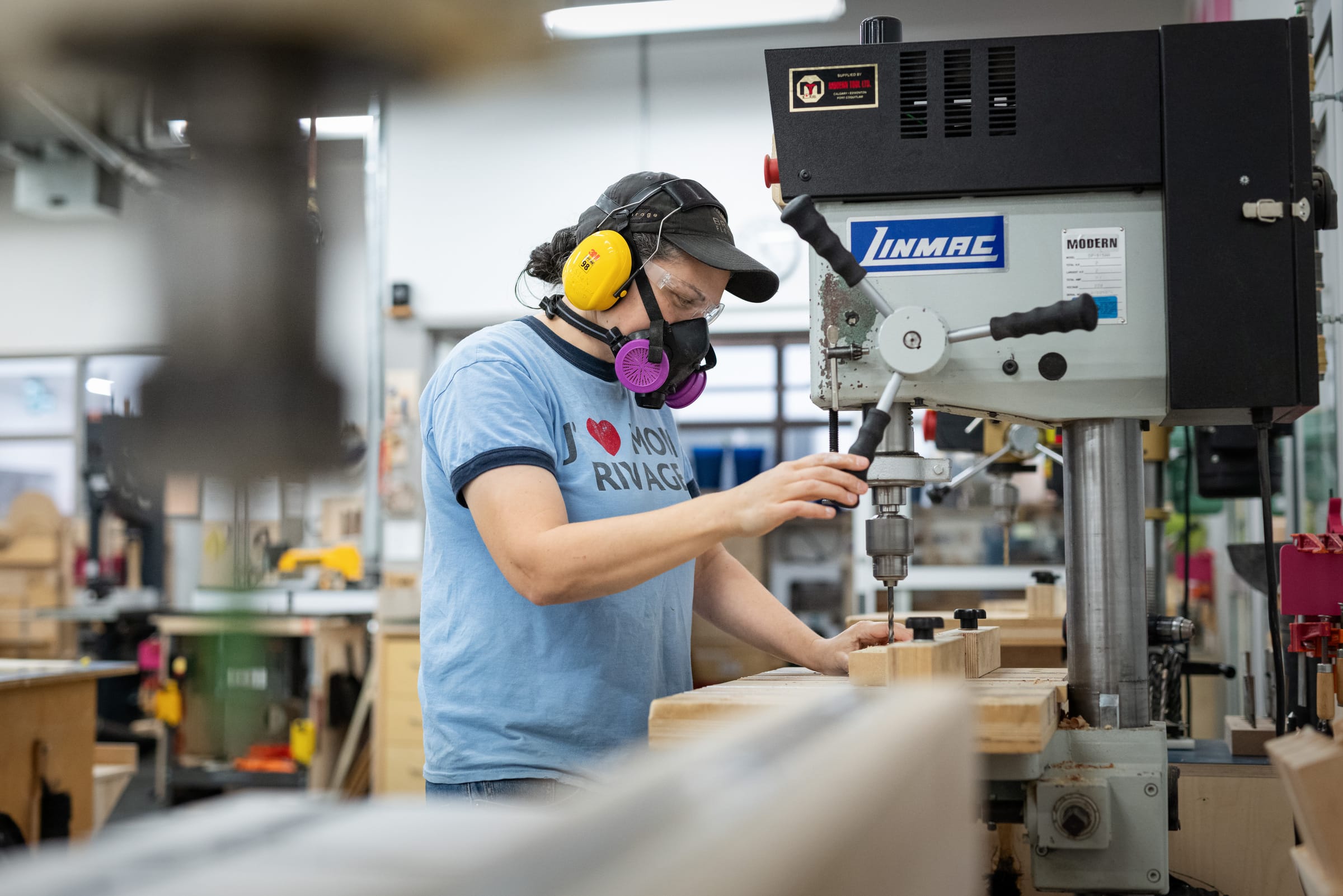 Technician using a drill press in the Design Wood Shop.