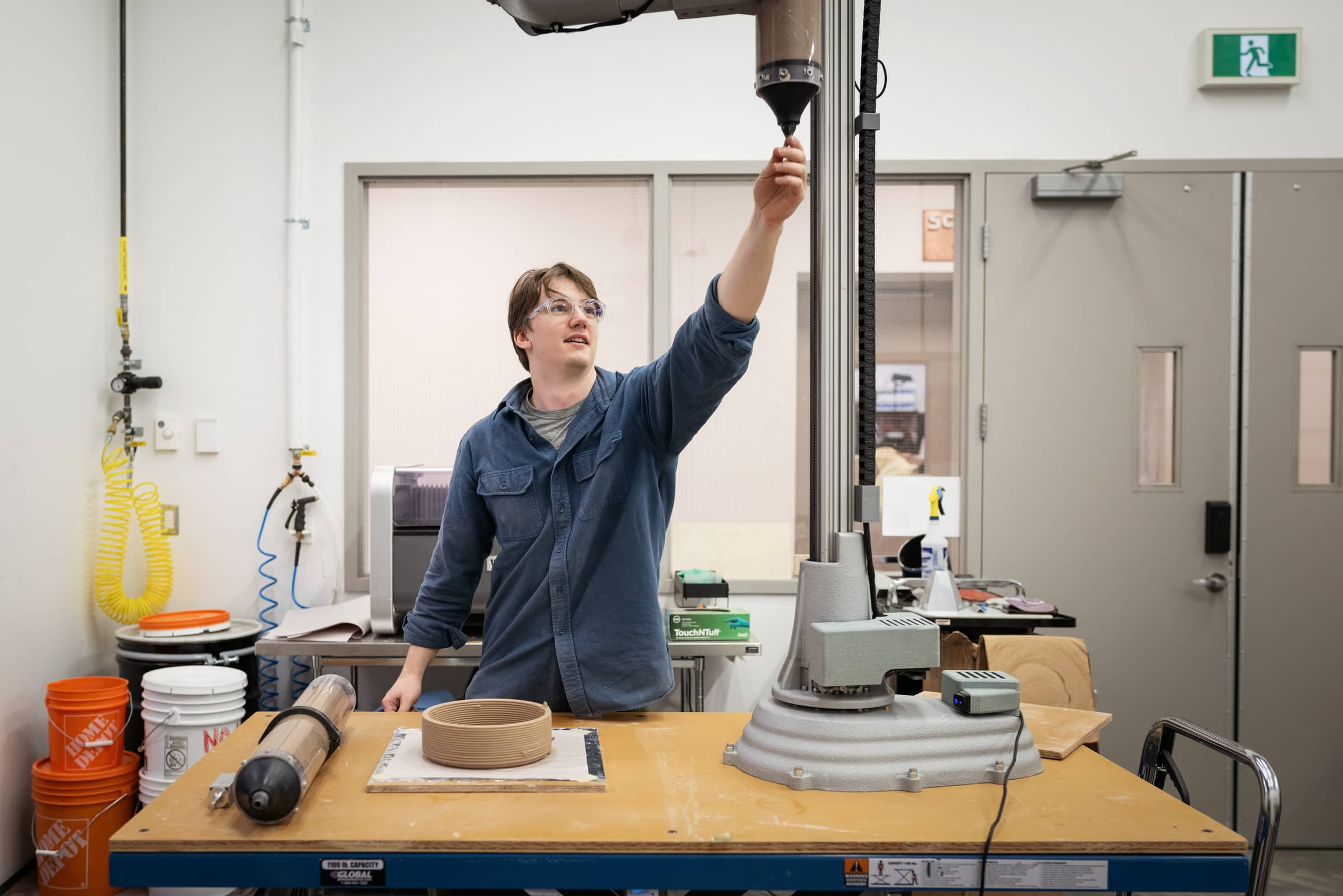 Student adjusting the nozzle of a 3D clay printer.