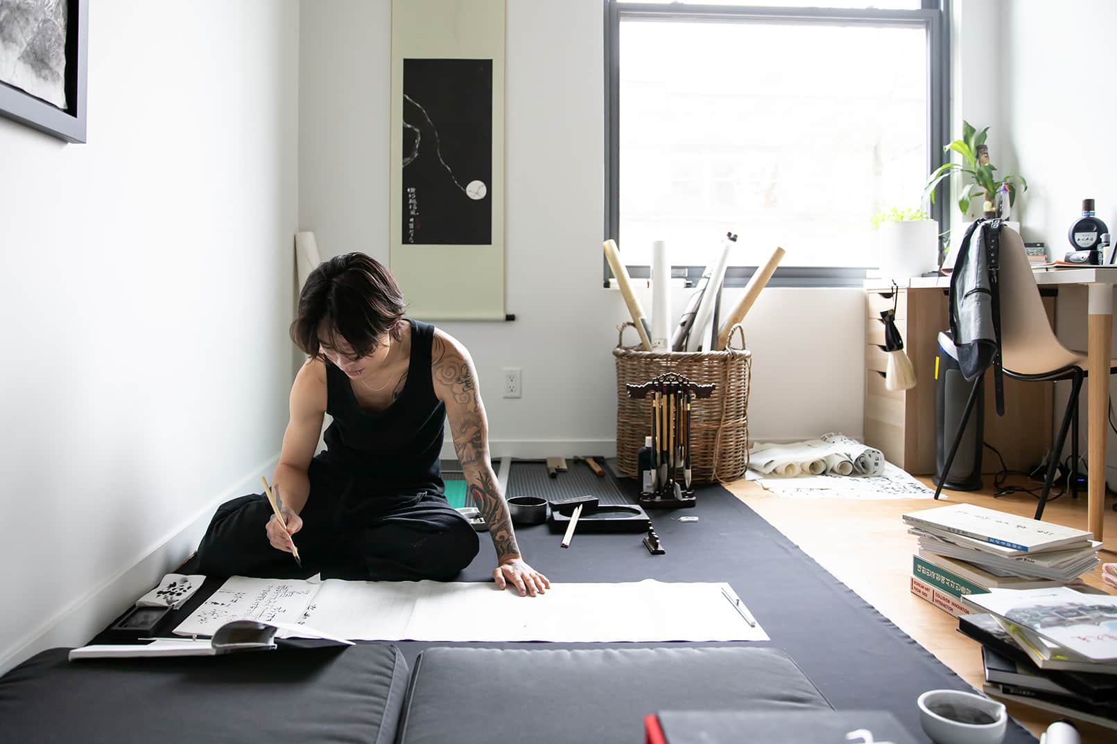 Person sitting cross-legged on the floor, practicing calligraphy with brushes and ink.