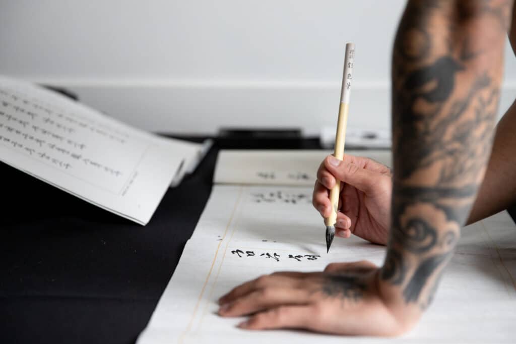 Close-up of a tattooed arm writing calligraphy with a brush.