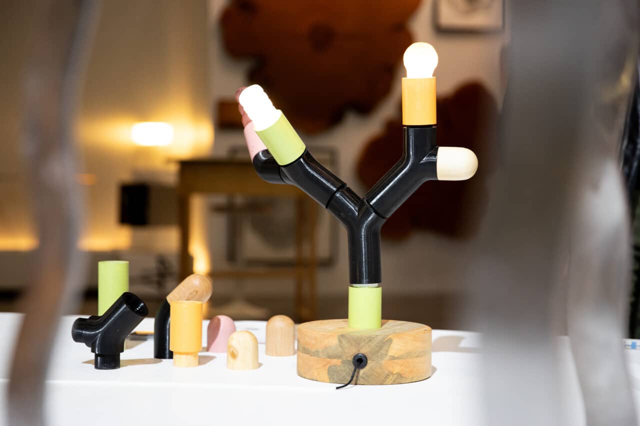 A modern table lamp with a wooden base and black branching structure, fitted with colorful socket covers and exposed light bulbs, surrounded by interchangeable lamp parts.