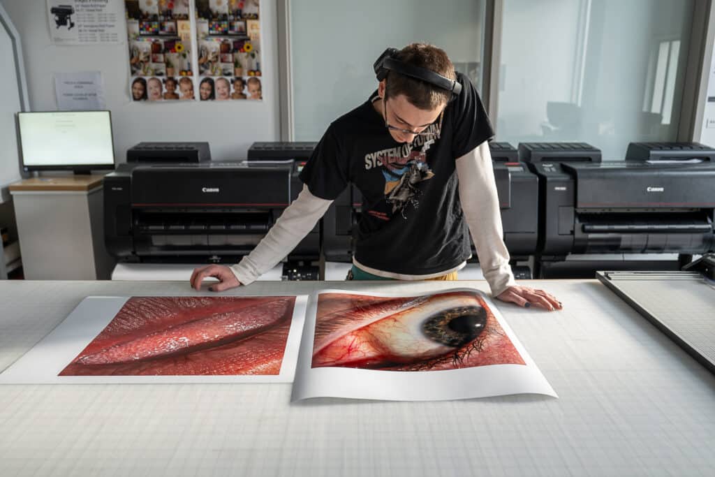 A person wearing headphones examining two large photographic prints on a table in a digital printing lab.