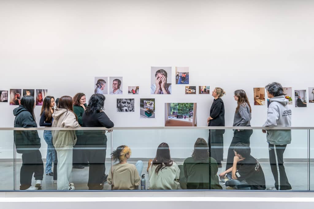 A group of students viewing a gallery wall installation of portrait photographs in an exhibition space.