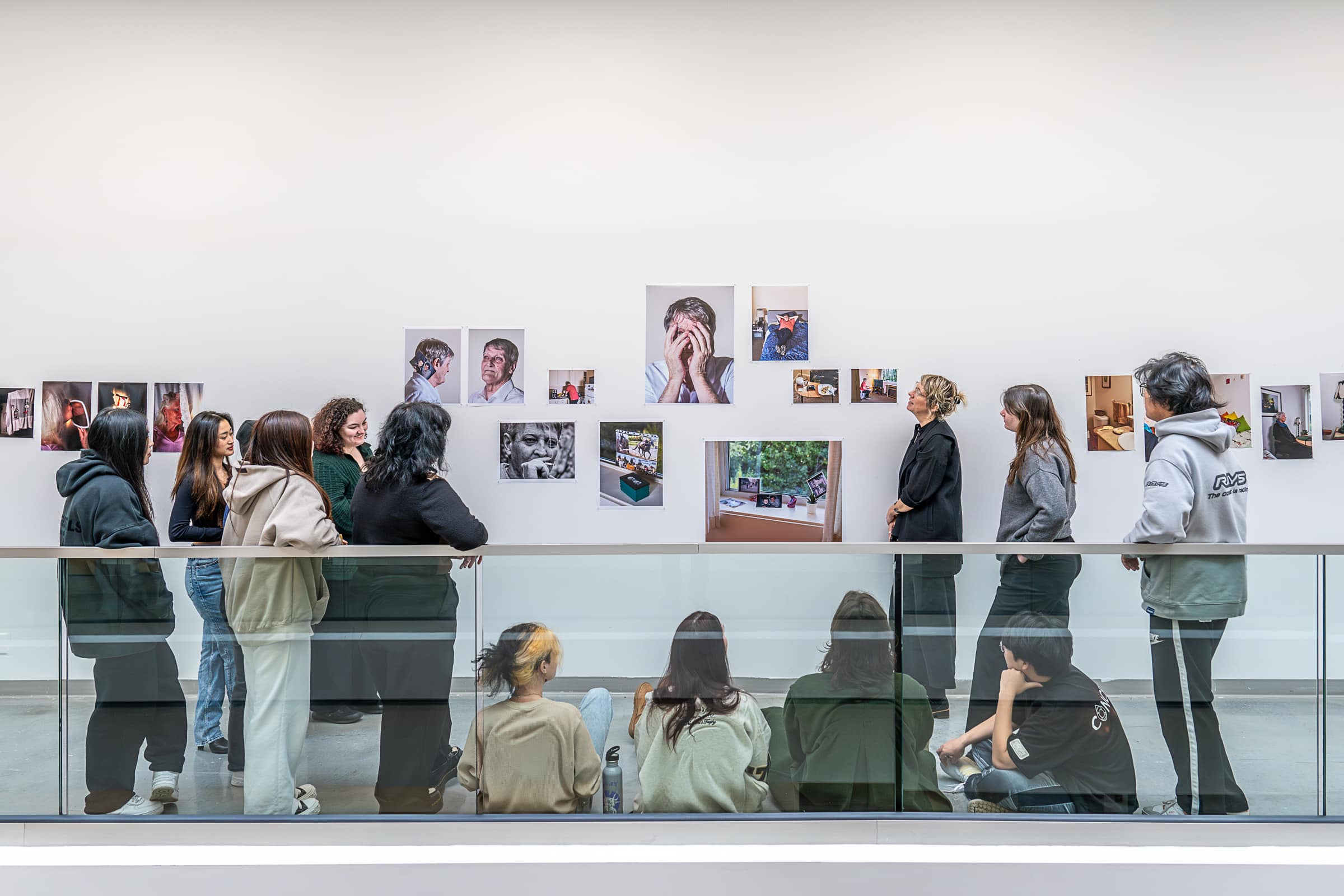 A group of students viewing a gallery wall installation of portrait photographs in an exhibition space.