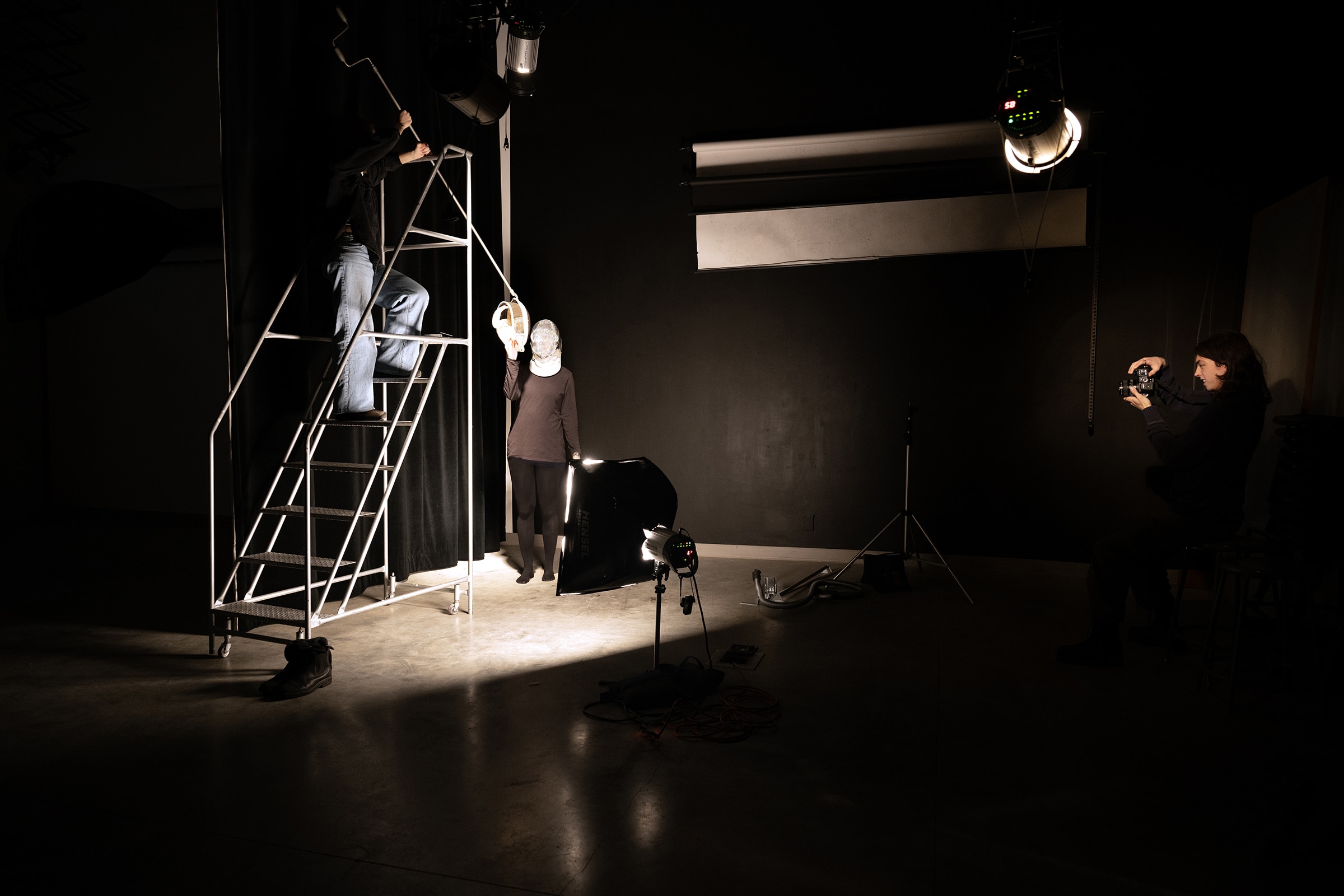 A dimly lit photo studio with multiple people adjusting lights and equipment to capture a staged portrait scene.