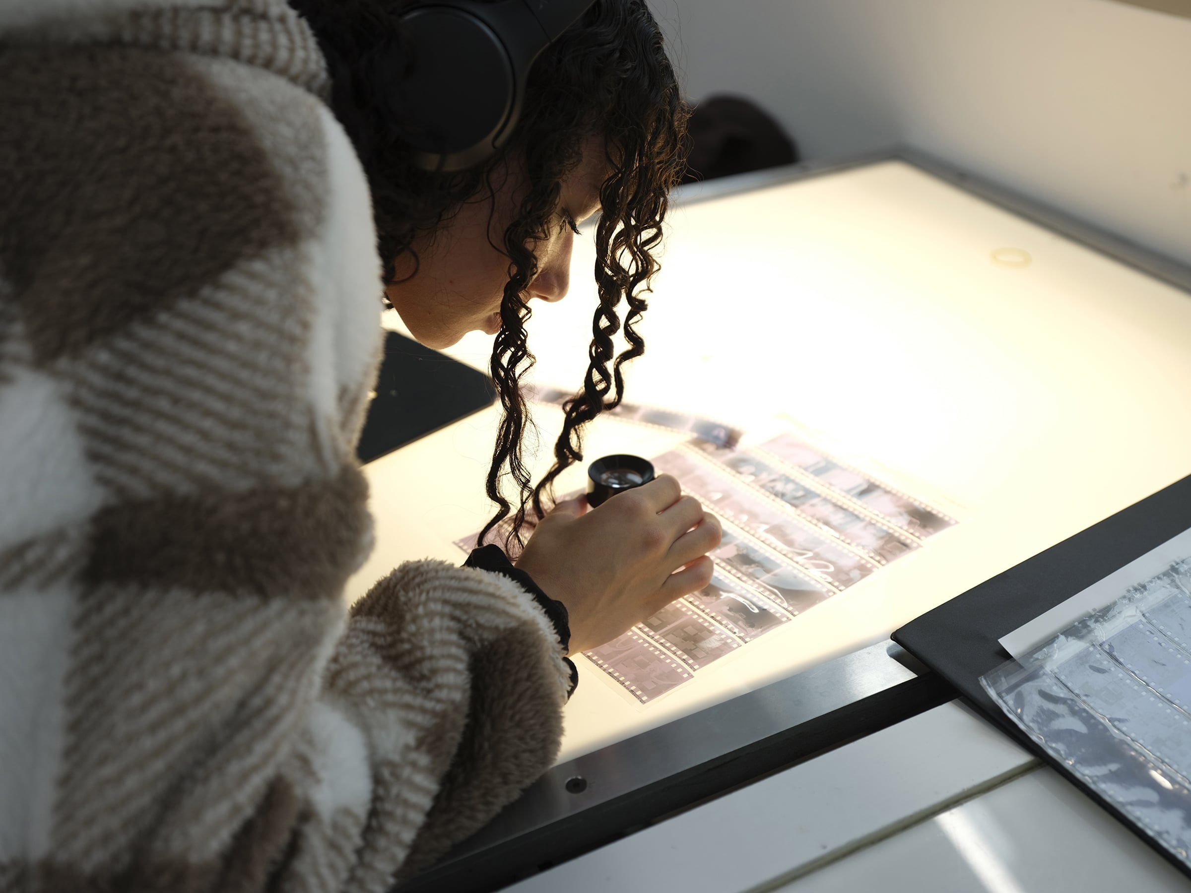 Person using a magnifier to closely examine film negatives on a light table.