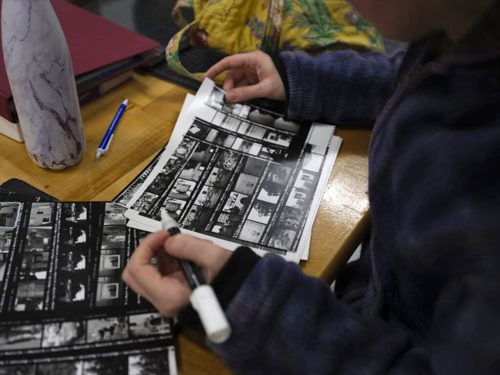 Person reviewing printed contact sheets of film negatives with a marker in hand.