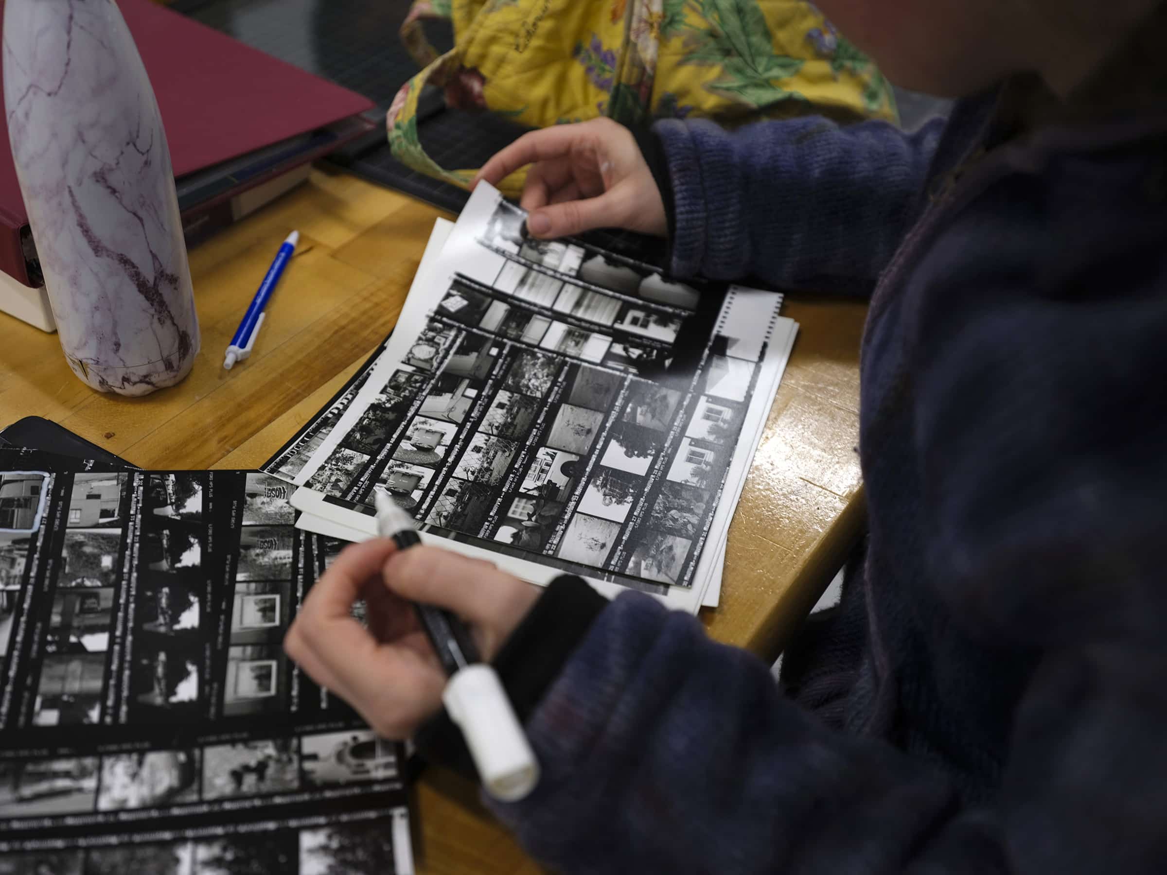 Person reviewing printed contact sheets of film negatives with a marker in hand.