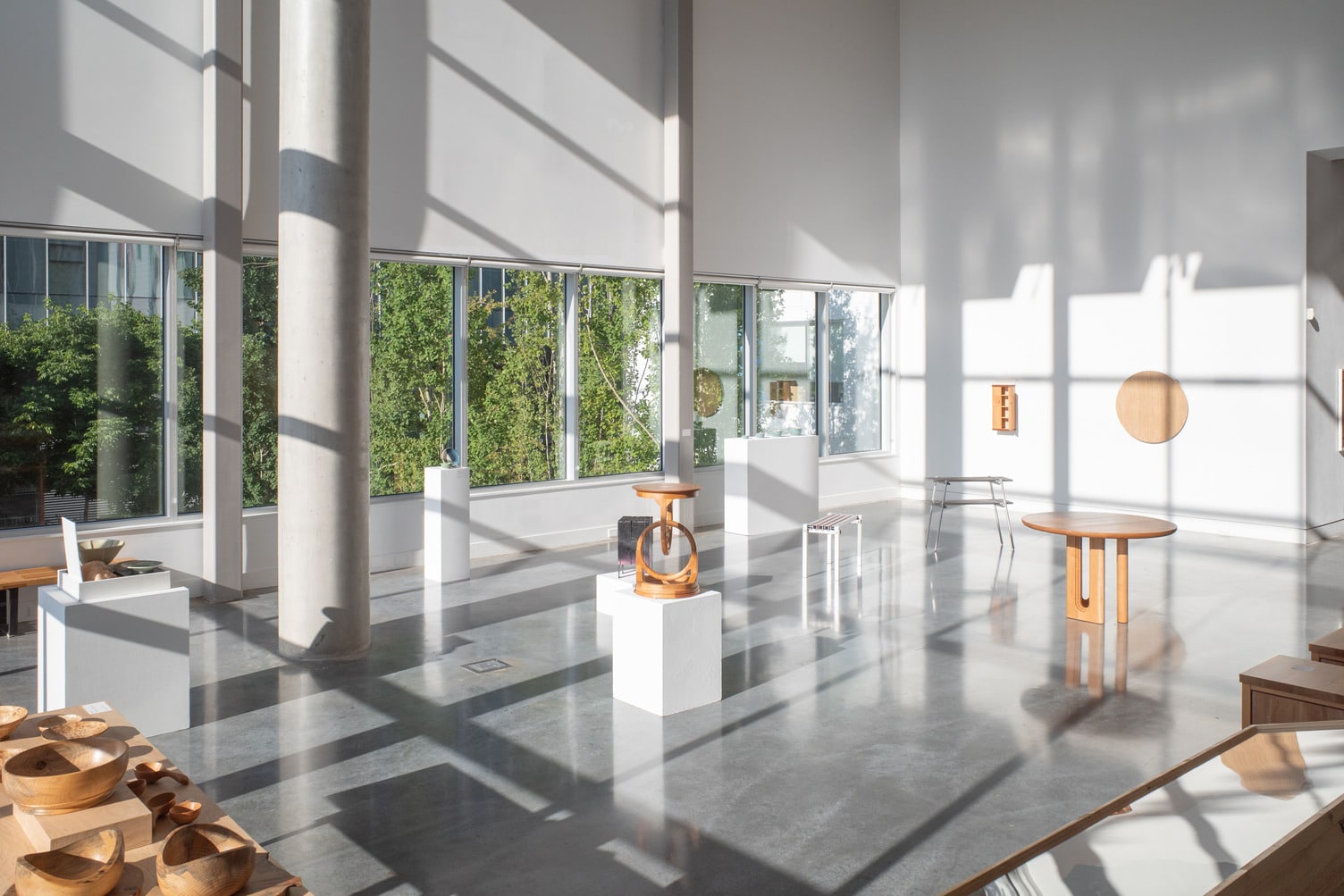 We see a bright, airy exhibition space bathed in sunlight filled with pieces made of light coloured wood.