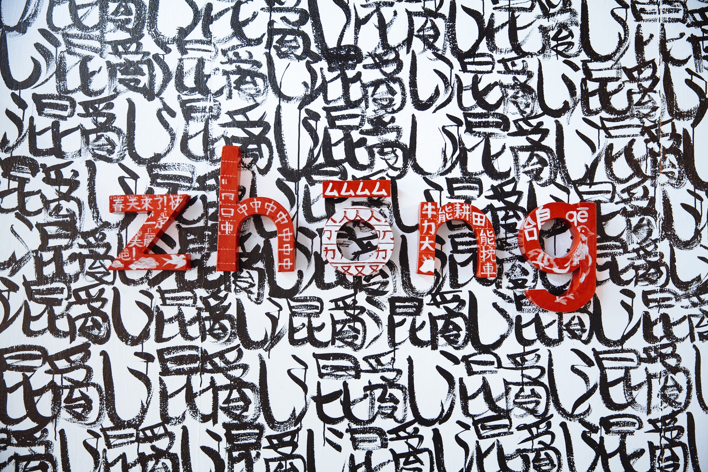 large artwork featuring the word “zhong” spelled out in red, three-dimensional letters covered with Chinese characters and patterns. The background is densely filled with repeating black calligraphy-like symbols.