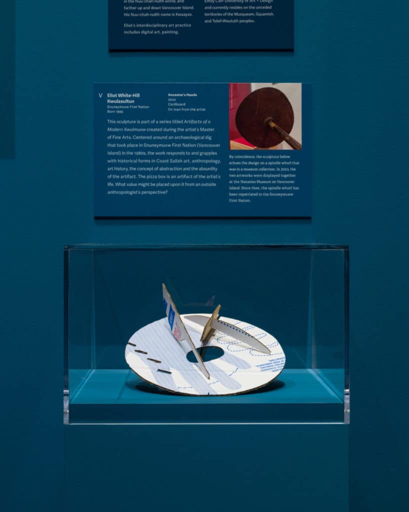Cardboard sculpture titled Ancestor’s Hands by Eliot White-Hill, displayed in a glass case with exhibition text above.