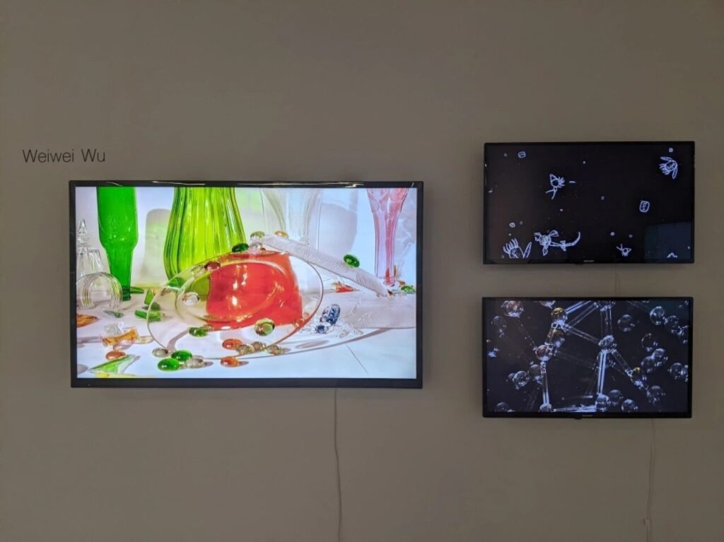 Three digital screens on a wall showing vibrant images of glass objects and abstract forms, with the name Weiwei Wu displayed.