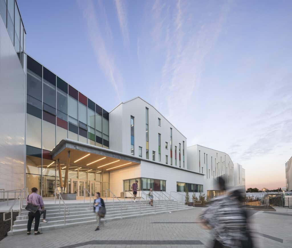Evening view of ECU’s main entrance, with people walking up the wide steps toward the glass-fronted building under a colorful sky.