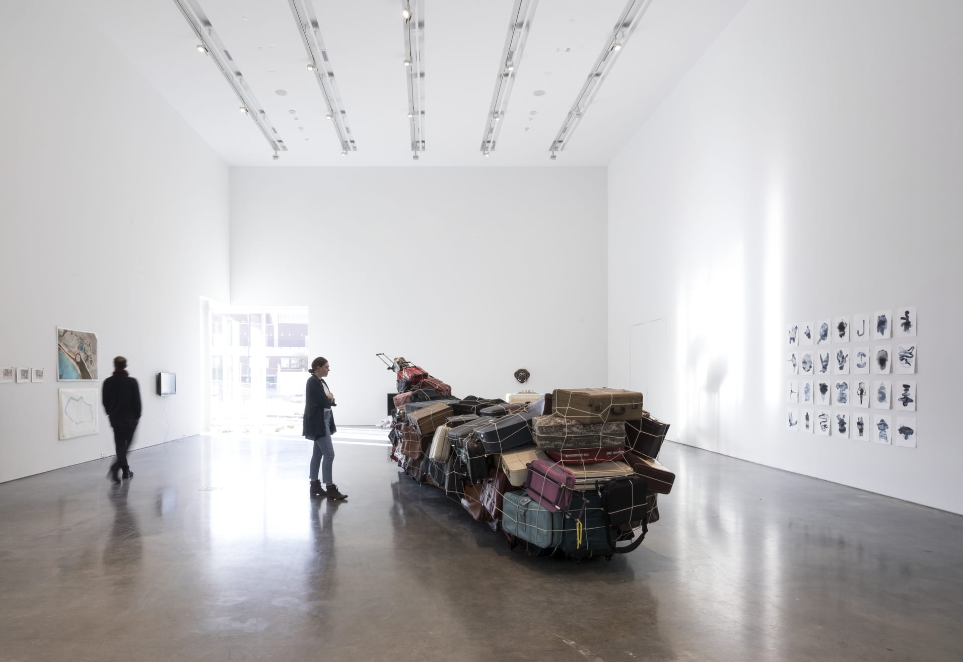 Gallery installation shot with students and visitors viewing artwork in a bright, open exhibition space.