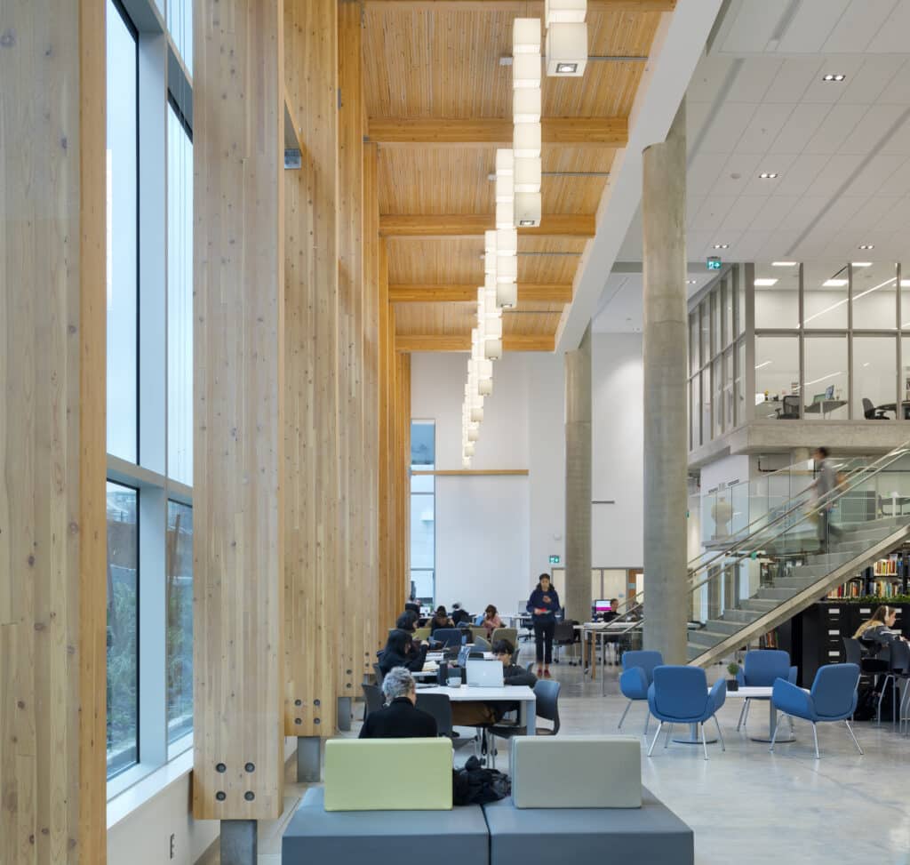Bright interior of ECU’s library commons, with wood beams, hanging lights, and students studying at long tables and lounge chairs.