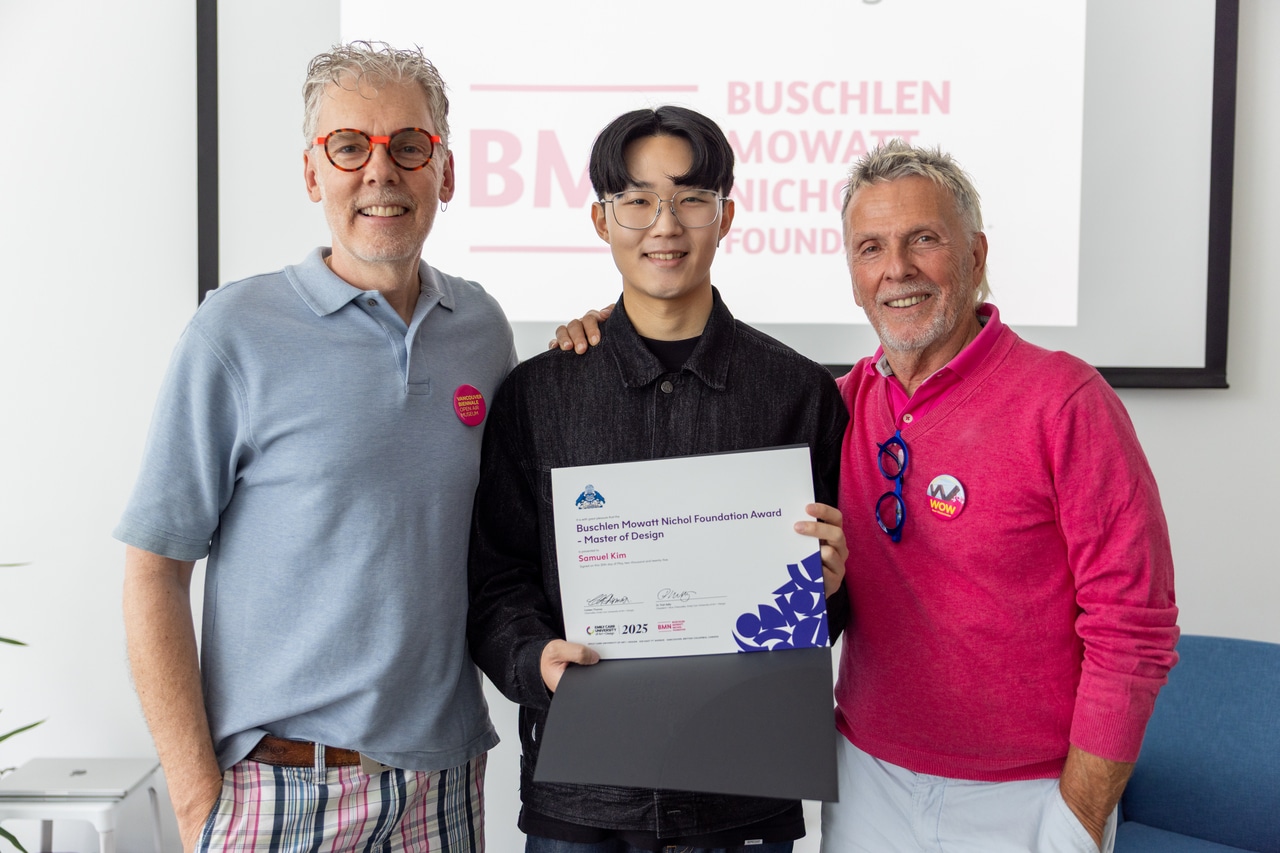 Three people smiling and posing together indoors, with the person in the middle holding a certificate. The certificate reads “Buschlen Mowatt Nichol Foundation Award – Master of Design, Samuel Kim.” The two men on either side are wearing colorful casual clothes and have their arms around the recipient. A presentation screen in the background shows the Buschlen Mowatt Nichol Foundation logo.