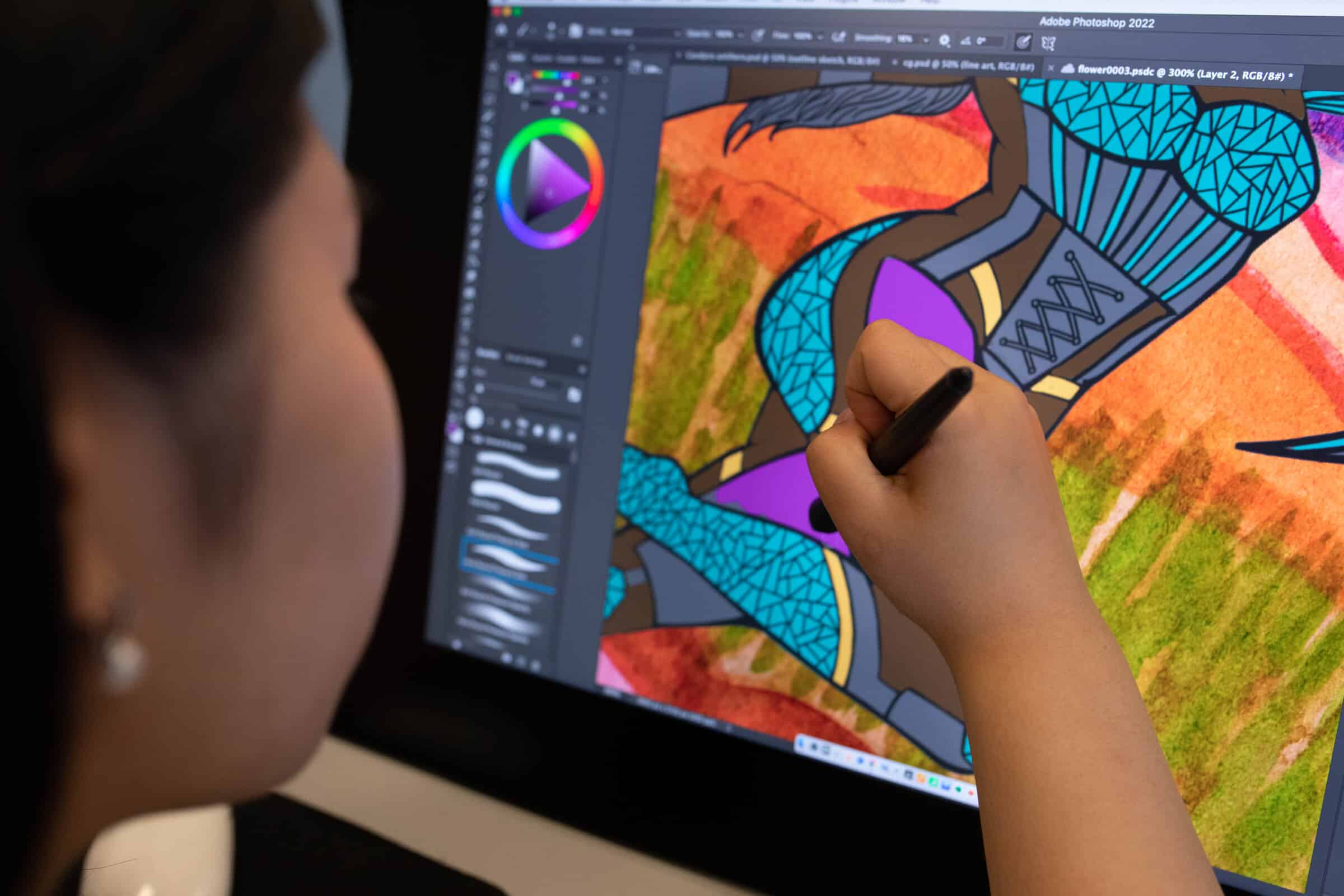 Close-up of a student’s hand using a stylus on a tablet, filling in vibrant purple and turquoise shapes on a digital illustration.