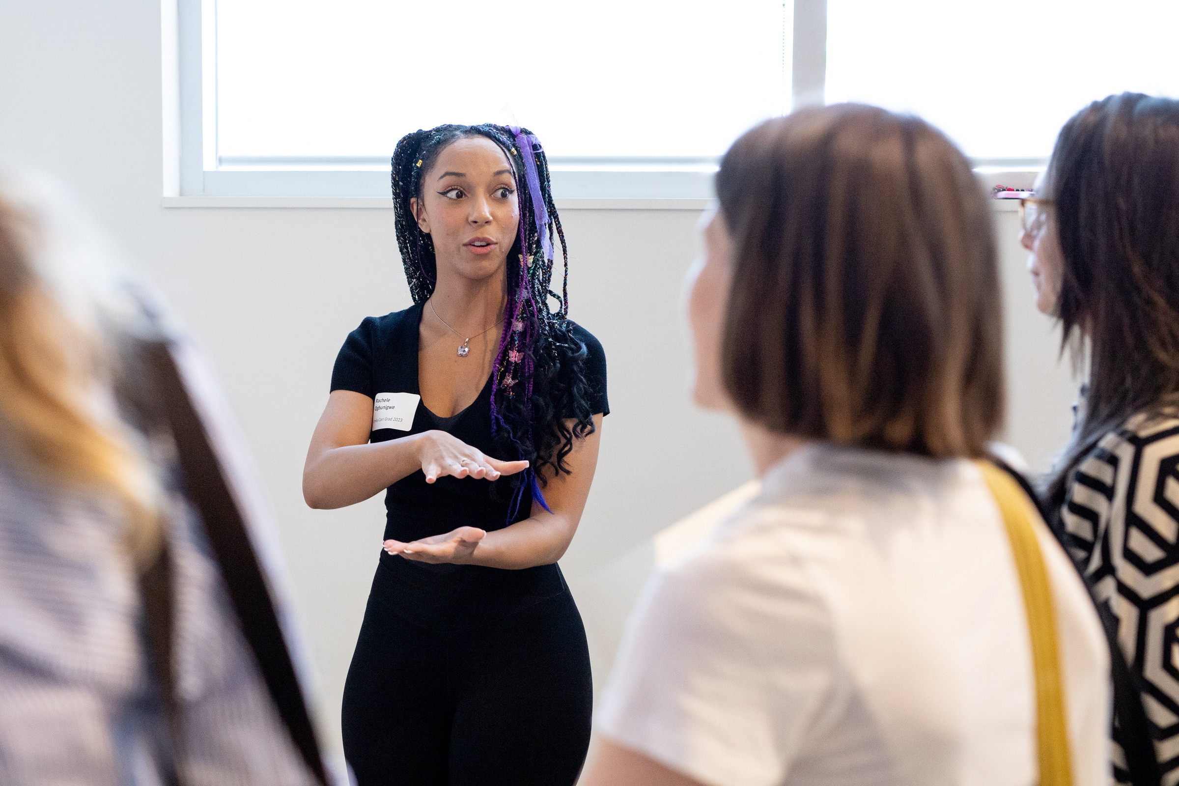 Student with braided hair gestures while speaking to a small group during a presentation.