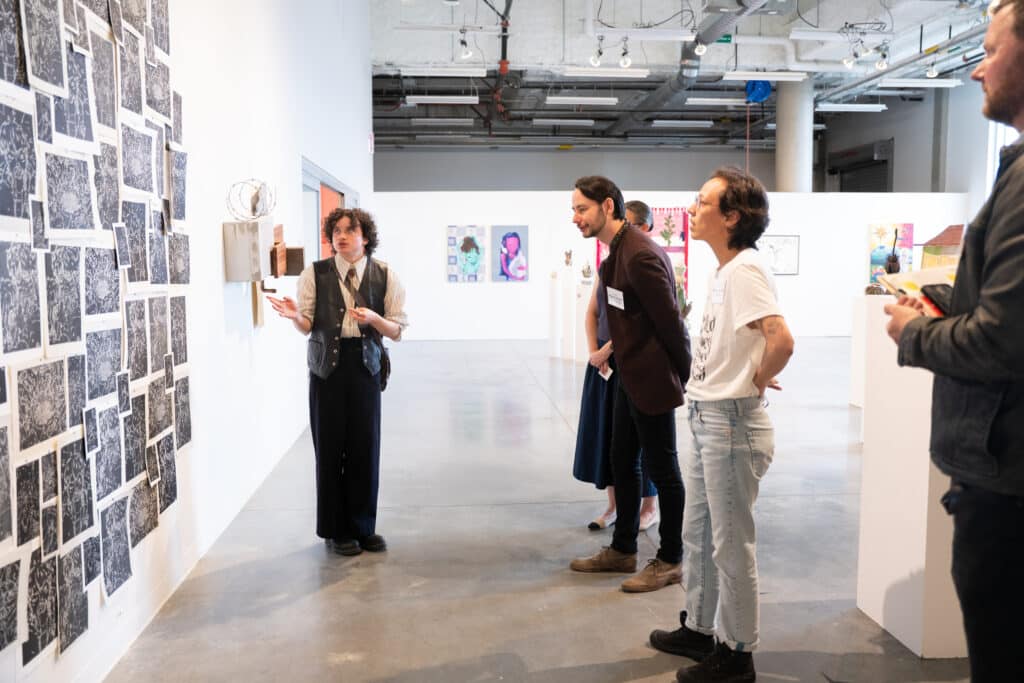 A student presents a wall installation of prints to a small audience during Crit Night at Emily Carr University.