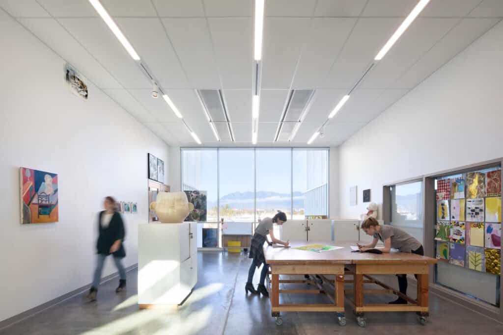 Bright studio with large windows, two students working at a central table surrounded by artwork.