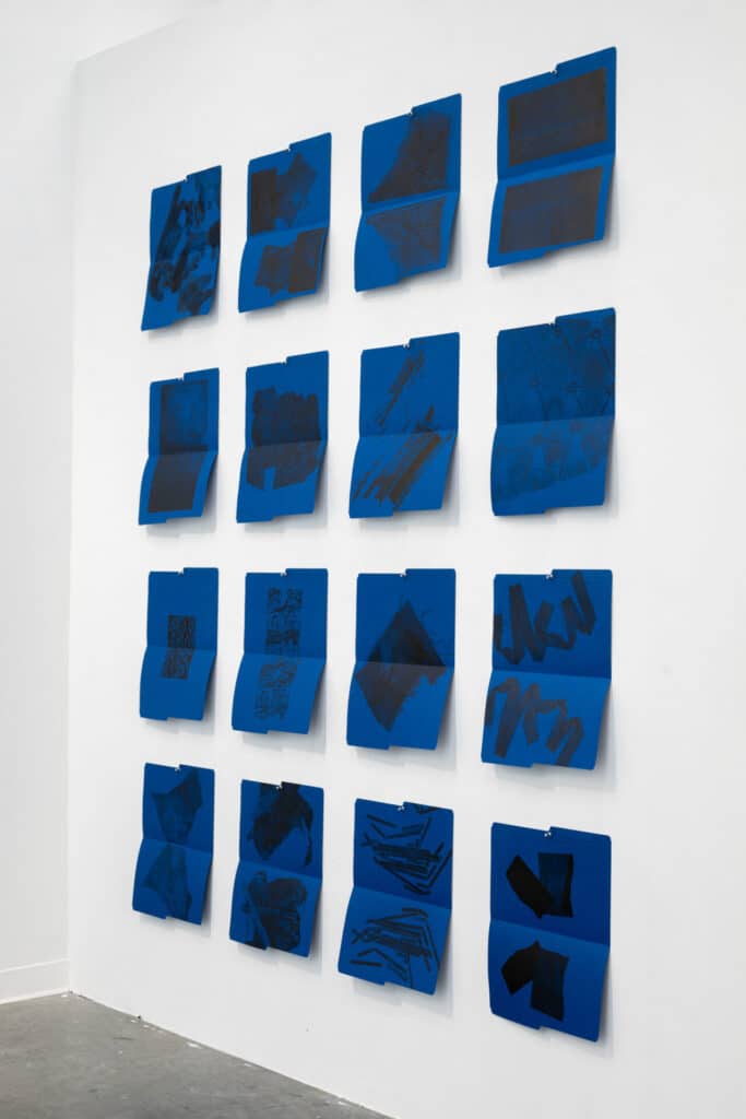 Grid of blue prints pinned to a white wall, each featuring abstract black patterns or shapes.