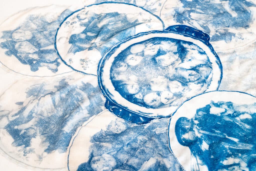 Fabric printed with overlapping blue circular images resembling food dishes, layered with stitched outlines.