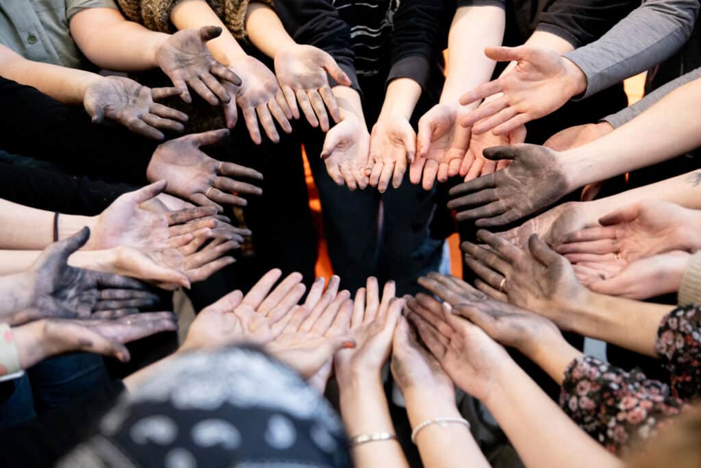 Group of students extend their hands in a circle, palms up, stained with charcoal after drawing.