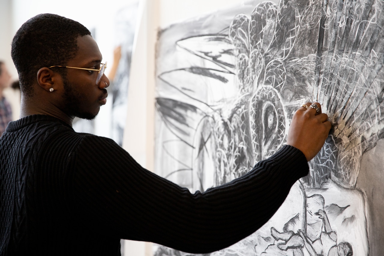 Student drawing with charcoal on large piece of white paper.