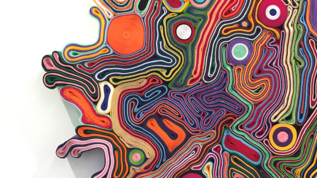 Close-up of a vibrant abstract artwork made from layers of rolled felt in swirling patterns of red, orange, green, purple, yellow, and pink.