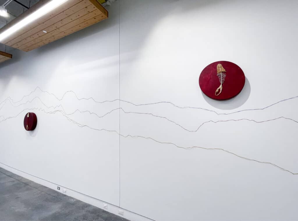 Two round red pieces with natural materials hang on a white wall with drawn mountain outlines.
