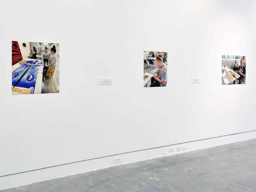 Three photographs of people working on art projects displayed on a white gallery wall.