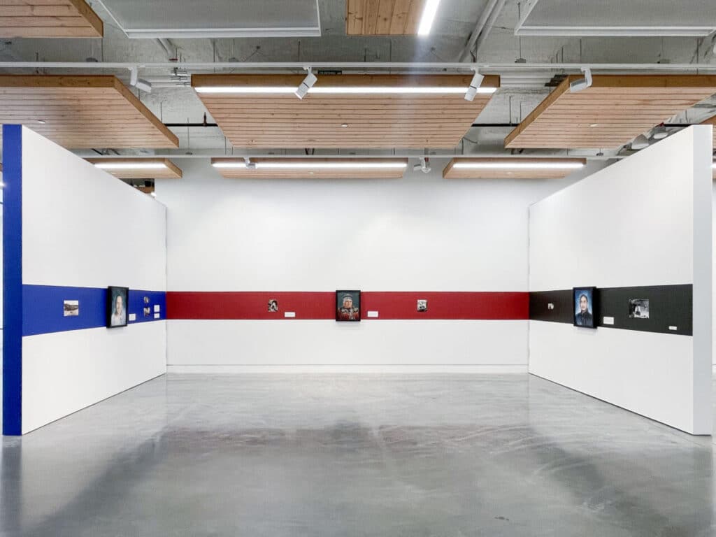 Small artworks and photographs arranged in coloured bands of blue, red and black across two gallery walls.