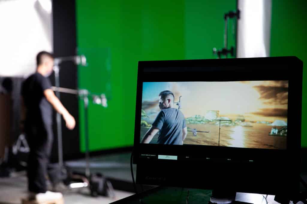 A student works in a studio with a green screen; a monitor shows the same student against a digital seascape background.