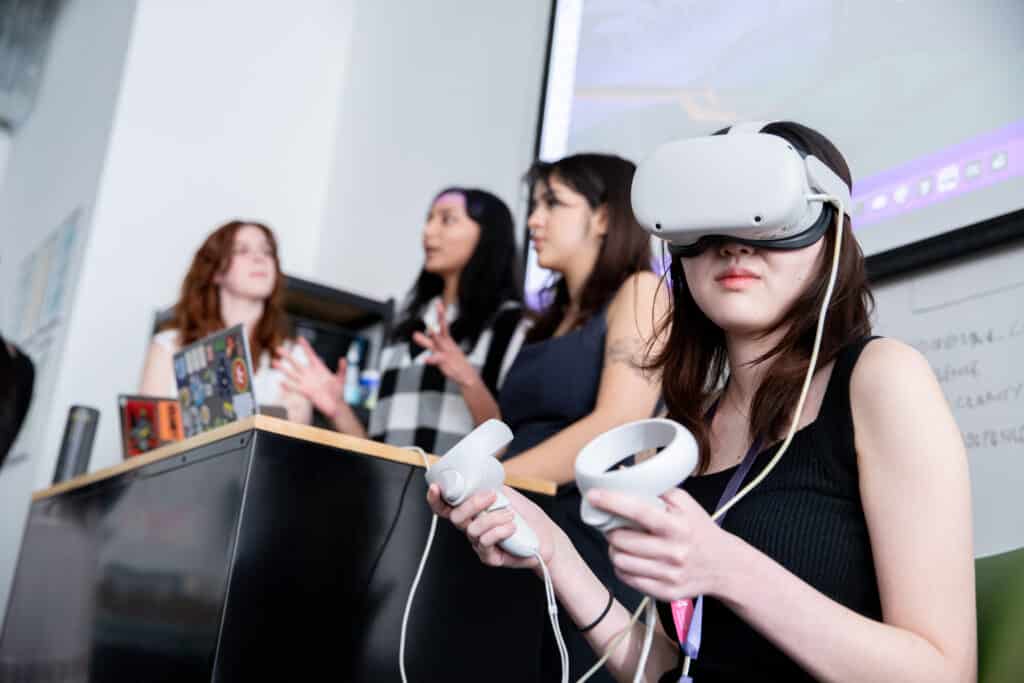 A student wearing a VR headset and controllers demonstrates an interactive project while peers present in the background at Emily Carr University.