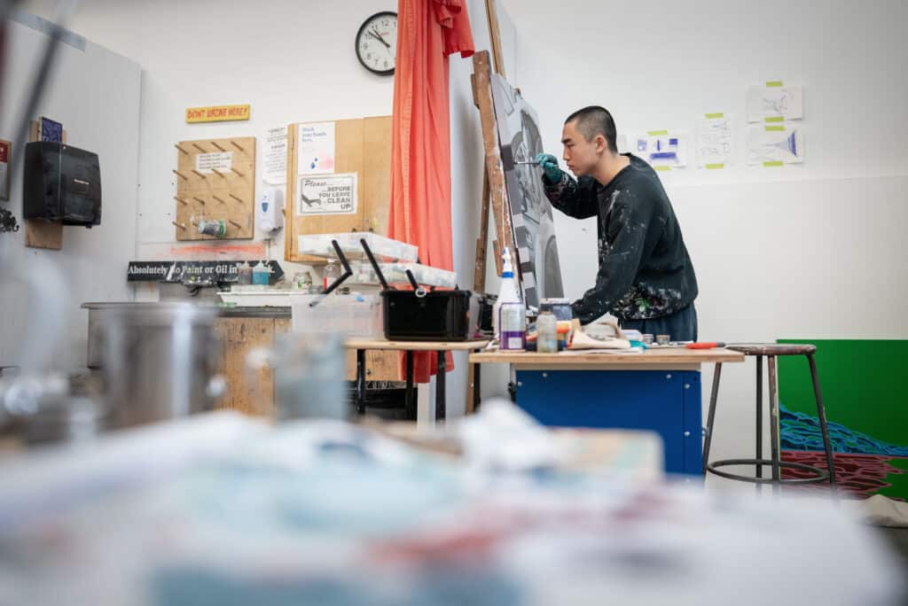 Student leaning over a painting propped up on an easel in the painting studios.