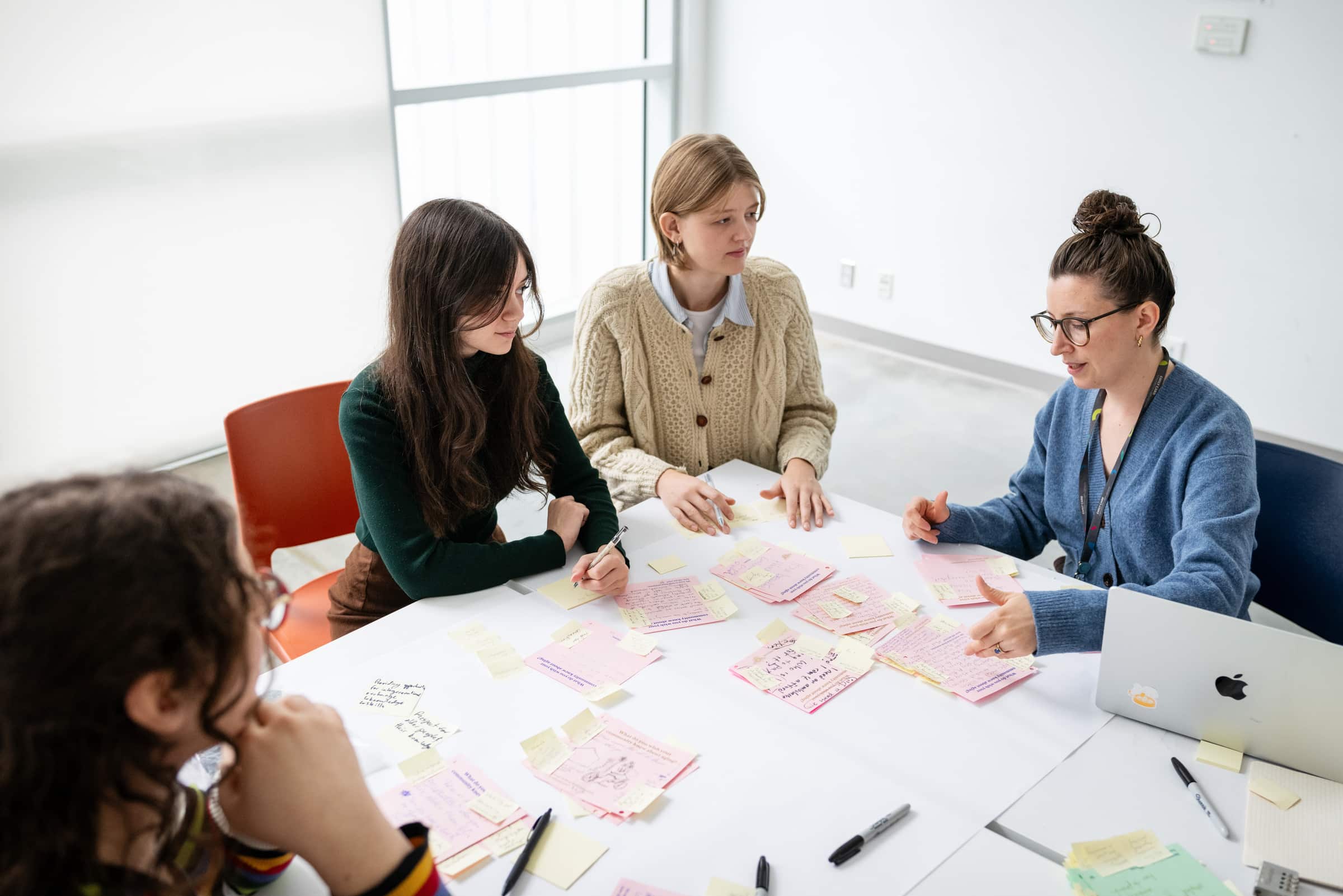 Group of four people collaborating at a table covered with sticky notes and sketches, engaged in brainstorming and discussion.