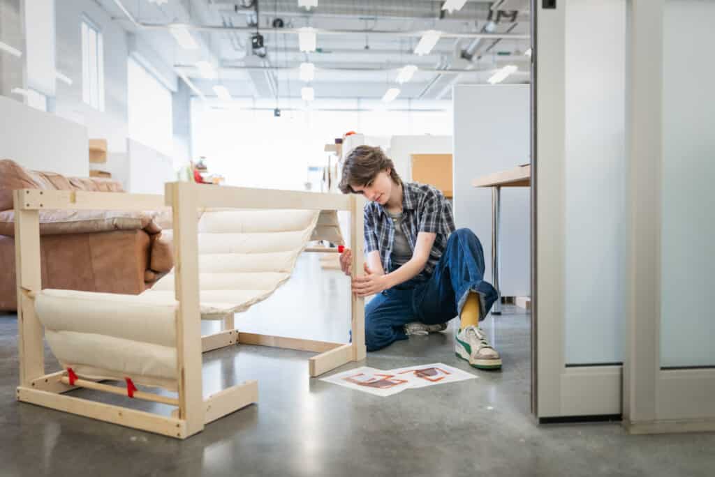 Student knealing, making adjustments to their wood and white fabric chair.