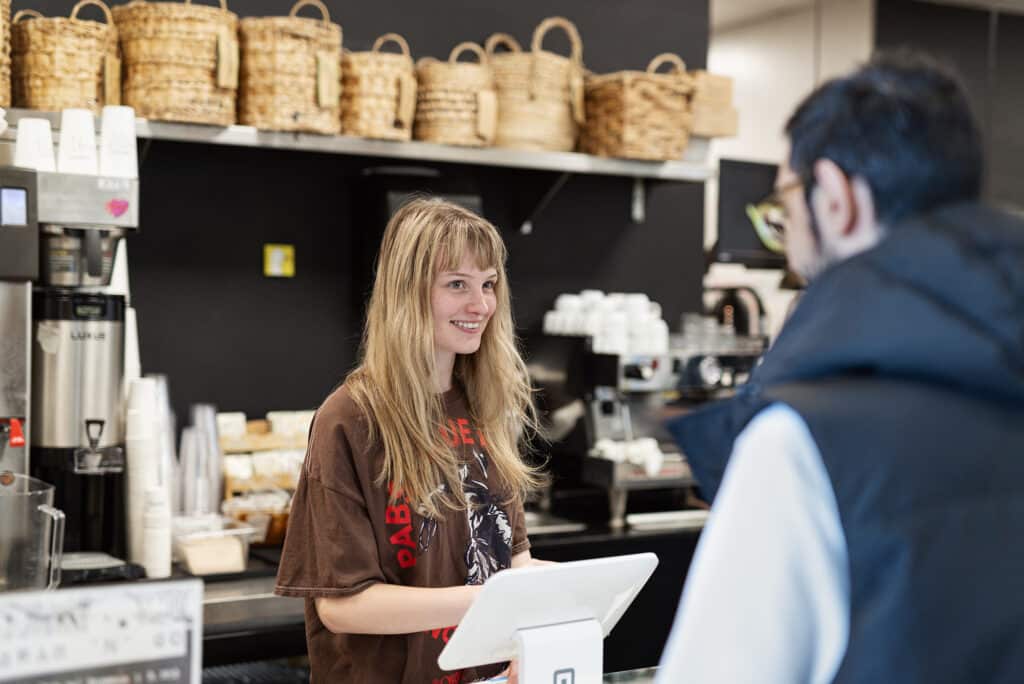 Barista smiles while serving a customer at the campus café counter.