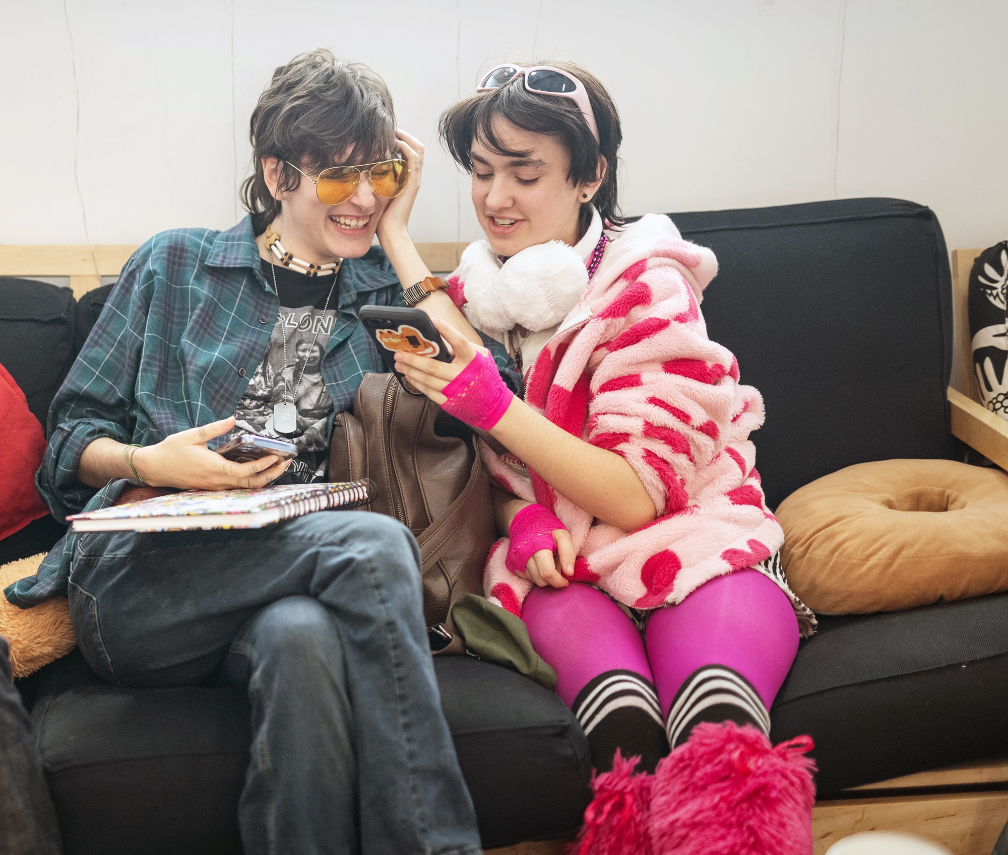 Two students in playful outfits sitting together on a couch, smiling while looking at a phone.